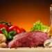 Ein Stück Rindfleisch liegt zwischen gesunden Nahrungsmitteln.