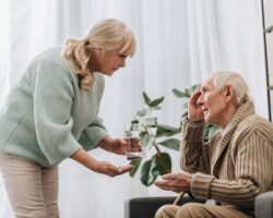 Eine Frau gibt einem älteren Mann ein Glas Wasser und Medikamente
