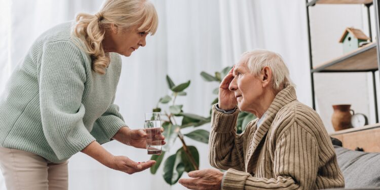 Eine Frau gibt einem älteren Mann ein Glas Wasser und Medikamente