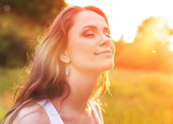 Junge Frau auf der Wiese genießt die Sonnenstrahlen während des Sonnenuntergangs