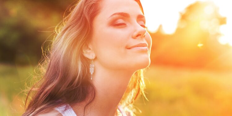 Een jonge vrouw in de wei geniet van de zon tijdens de zonsondergang