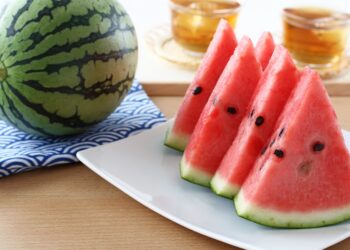 Eine ganze Wassermelone auf einem Tisch neben einem Teller mit geschnittenen Wassermelonenstücken