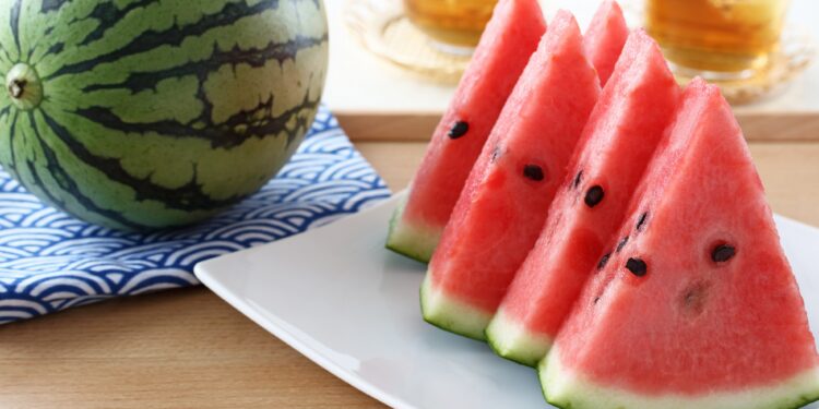 Eine ganze Wassermelone auf einem Tisch neben einem Teller mit geschnittenen Wassermelonenstücken