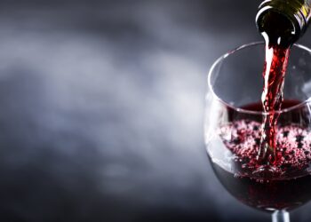 Aus einer Flasche wird Rotwein in ein Glas geschenkt
