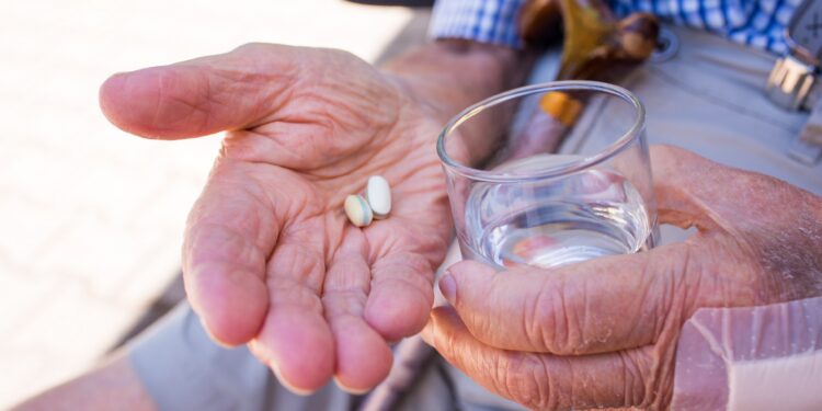 Senior mit zwei Tabletten und einem Glas Wasser in seinen Händen