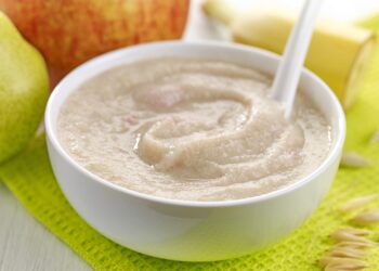 Eine Schüssel mit Babybrei vor etwa Obst auf einem Tisch