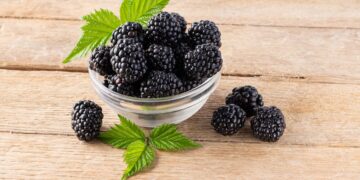 Brombeeren und Blätter in einer Glasschüssel auf einem Holztisch