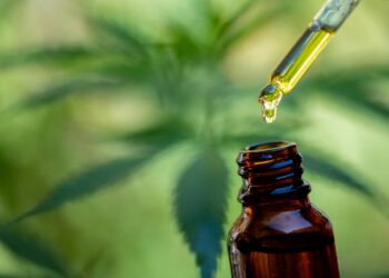 Pipette und Fläschchen mit einem Cannabisblatt im Hintergrund.
