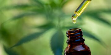 Pipette und Fläschchen mit einem Cannabisblatt im Hintergrund.