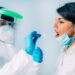 Medizinische Fachkraft in Schutzkleidung nimmt bei einer jungen Frau einen Rachenabstrich für einen Corona-Test