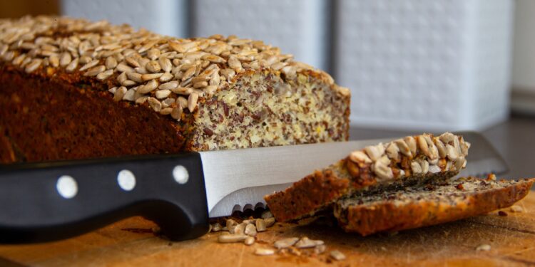 Eiweißbrot mit Brotmesser und zwei Brotscheiben auf einem Holzbrett