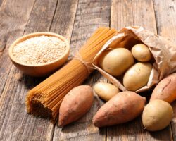 Kohlenhydratreiche Lebensmittel wie Nudeln und Kartoffeln auf einem Holztisch