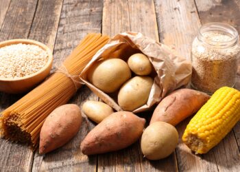 Kohlenhydratreiche Lebensmittel wie Nudeln und Kartoffeln auf einem Holztisch