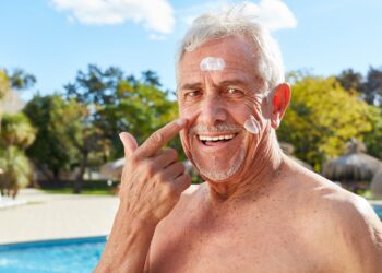 Älterer Mann cremt sein Gesicht mit Sonnenschutzmittel ein