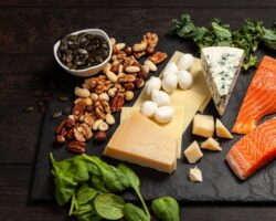 Verschiedene proteinreiche Lebensmittel wie Fisch und Käse auf einer dunklen Platte