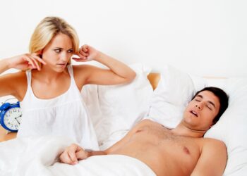 Eine Frau hält sich die Ohren zu, während ein Mann im Bett schläft.
