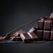 Schokoladenstücke und Schokoladenpulver in einem kleinen Löffel vor dunklem Hintergrund