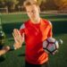 Ein Fußballer mit eine Fußball in der Hand weist eine angebotene Flasche Bier zurück