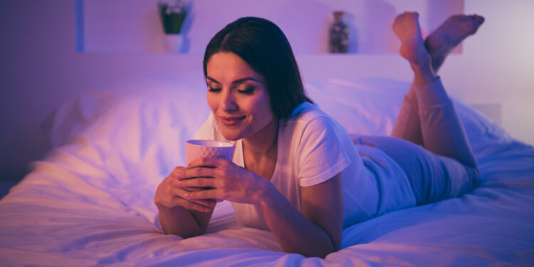 Frau liegt im Bett und hält eine Tasse