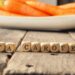 Holzwürfel mit dem englischen Wort für Beta-Carotin vor einem Teller mit Karotten auf einem Holztisch