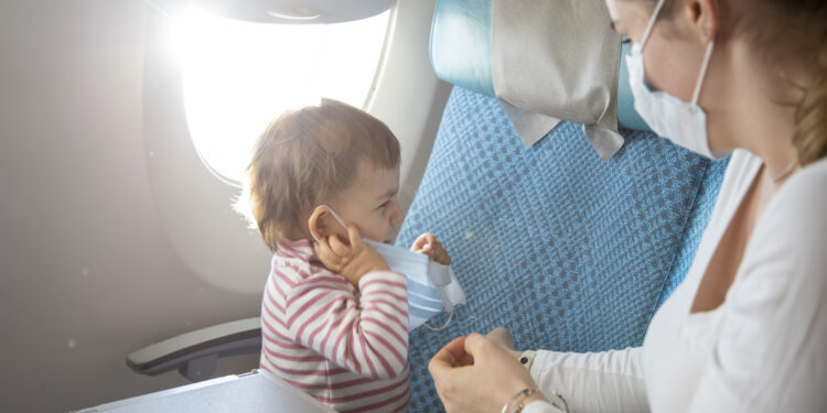 Frau mit Mund-Nasen-Schutz sitzt neben ihrem Kind im Flugzeug