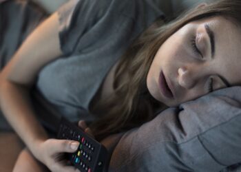 Junge Frau schläft mit Fernbedienung in der Hand