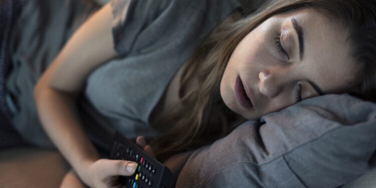Junge Frau schläft mit Fernbedienung in der Hand