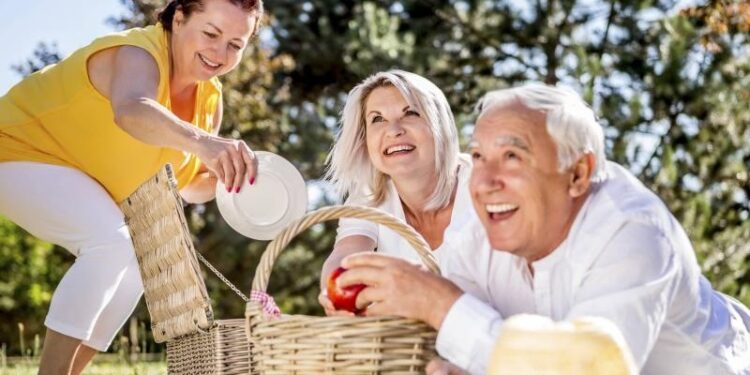 Drei ältere Personen machen ein Picknick auf einer Wiese.