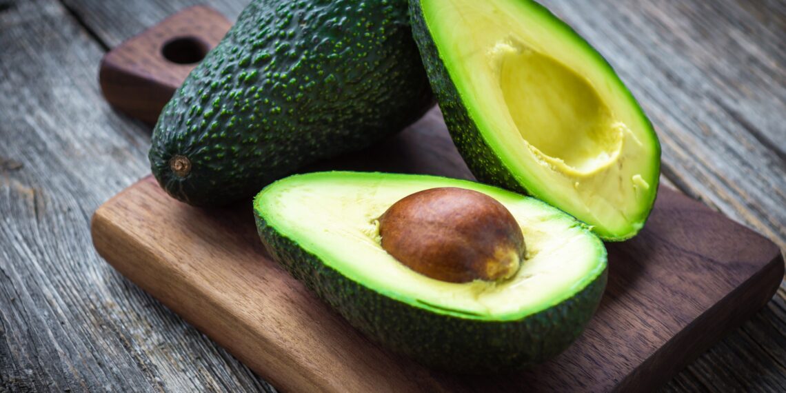 Eine ganze und eine aufgeschnittene Avocado auf einem Holzbrett
