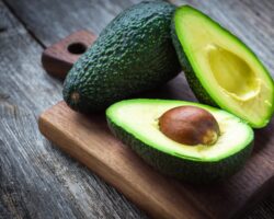 Eine ganze und eine aufgeschnittene Avocado auf einem Holzbrett