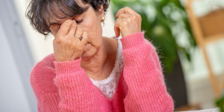 Erschöpfte Seniorin reibt sich die Nasenwurzel