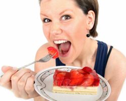 Frau mit weit geöffnetem Mund hält einen Teller mit einem Stück Erdbeerkuchen