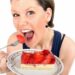 Frau mit weit geöffnetem Mund hält einen Teller mit einem Stück Erdbeerkuchen