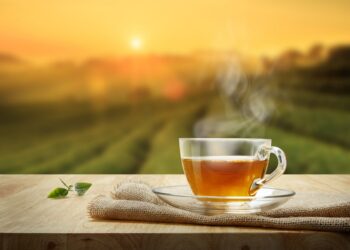 Tasse heißer Tee und Teeblatt auf einem Holztisch mit Teeplantage im Hintergrund