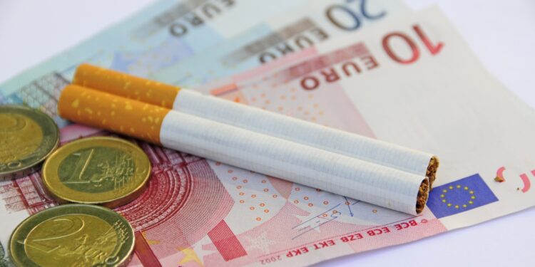 Zwei Zigaretten auf Euro-Geldscheinen und daneben Münzen