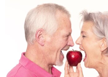 Ein älteres Pärchen beißt von zwei Seiten in einen Apfel.