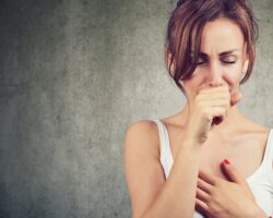 Frau hustet und fasst sich an den Brustkorb.