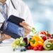 Obst und Gemüse und ein Maßband auf einem Tisch vor einem Arzt mit einem Blutdruckmessgerät