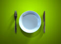 Ein leerer Teller, ein Messer und eine Gabel auf einer grünen Oberfläche