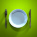Ein leerer Teller, ein Messer und eine Gabel auf einer grünen Oberfläche