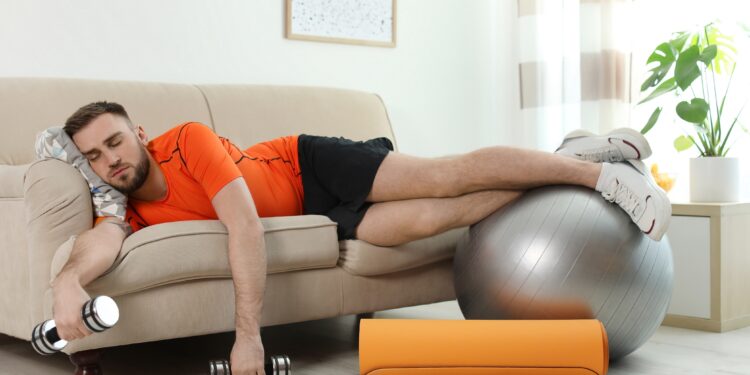 Mann mit Trainingsgeräten schläft auf dem Sofa.