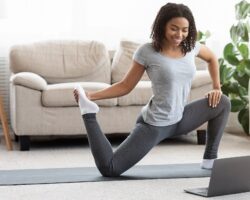 Frau trainiert im Wohnzimmer vor dem Laptop auf Yogamatte