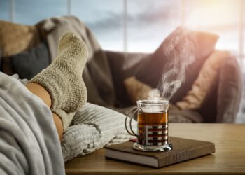 Eine Tasse heißer Tee neben Füße in dicken Socken auf einem Tisch