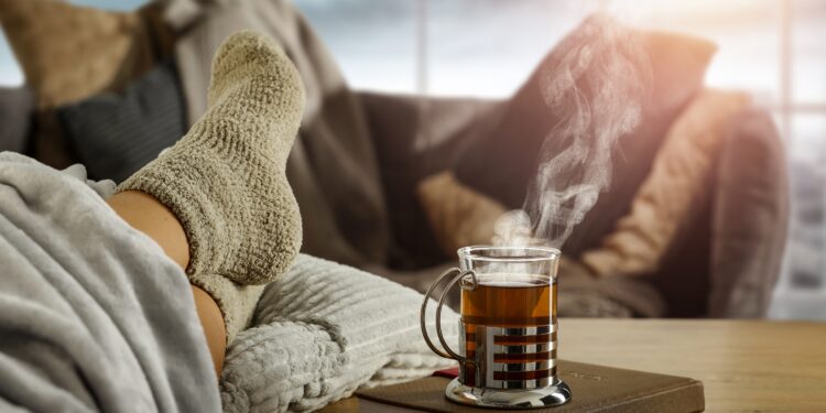 Eine Tasse heißer Tee neben Füße in dicken Socken auf einem Tisch