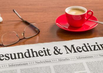 Auf einem Schreibtisch befinden sich eine Brille, eine Zeitung und eine Tasse Kaffee.