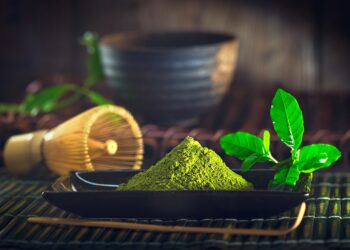 Ein schwarzes Schälchen mit Matcha-Pulver steht auf einem Tisch.