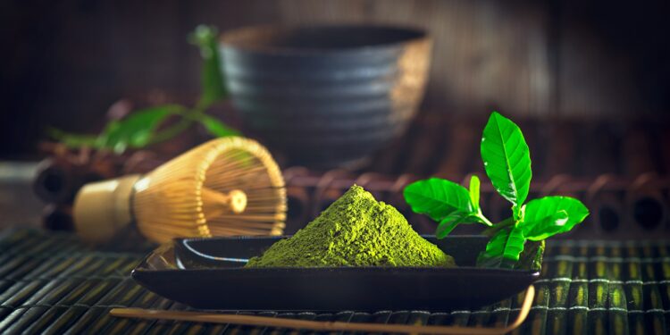 Ein schwarzes Schälchen mit Matcha-Pulver steht auf einem Tisch.