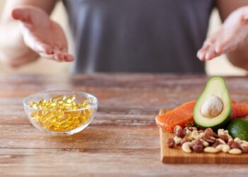 Auf einem Tisch steht ein Teller mit gesunden Lebensmitteln und eine Schale voll Vitaminpräparaten.