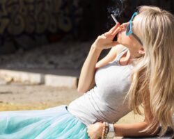 Junge Frau liegt rauchend in der Sonne.