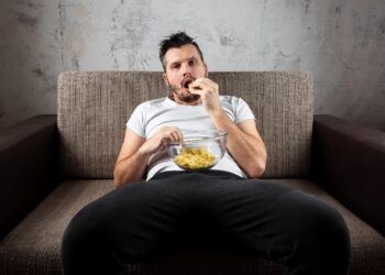 Mann vor dem Fernseher auf Sofa mit Chips.